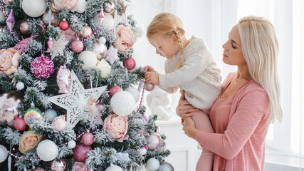 Mom and daughter decorate the Christmas pink tree indoors.