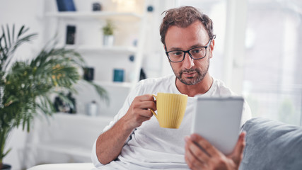 Wall Mural - Man holding tablet, surfing online and drinking coffee.