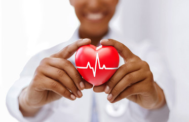 health, medicine and charity concept - african american female doctor holding red heart with ecg line