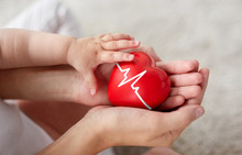 Family, Charity And Health Concept - Close Up Of Little Baby And Mother's Hands Holding Red Heart With Ecg Line