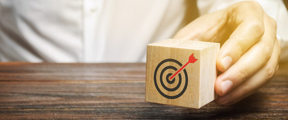 A businessman holds in his hands a wooden block with a target symbol. The concept of achieving business goals. Execution of a business plan. Purposefulness. Goal. Planning. Strategy