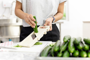 Woman slicing cucumber with vegetable slicer for salad.