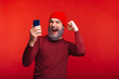 © Vulp - Photo of cheerful man with white beard and red cap looking at smartphone and celebrating success