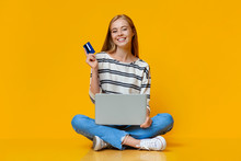 Cheerful Girl Holding Credit Card And Laptop, Sitting On Floor