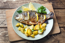 Baked Fish Carp With Lemon Greens And Potatoes On A Plate. Wooden Background.