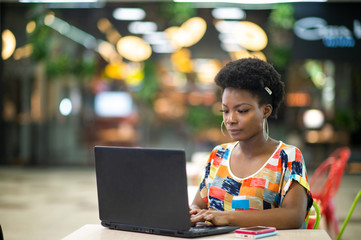 Wall Mural - Beautiful Young Dark Skinned Freelancer Woman Using Laptop Computer Sitting At Cafe Table.  Freelance Work Concept.