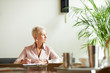 © AnnaStills - Mature businesswoman with short blond hair looking away while working at the table at office