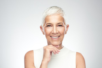 Beautiful smiling senior woman with short gray hair posing in front of gray background. Beauty photography.