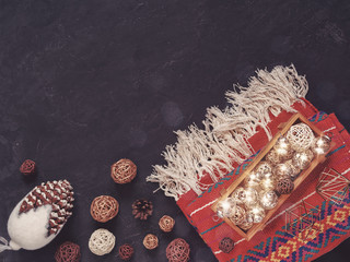 Christmas composition. Glass balls are in a wooden box on a red knitted blanket. Nearby are wicker balls and a large fir cone. Black stone background. Flat lay.