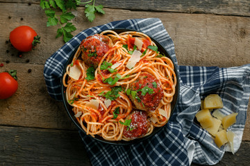 Wall Mural - Pasta with meatballs, parmesan and tomato sauce in a clay bowl. Homemade Italian spaghetti on a rustic wooden table. Top view shot.