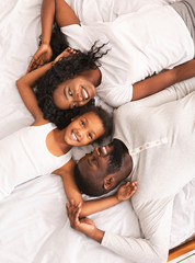 Wall Mural - Little black girl and her parents lying on bed together