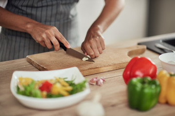 Wall Mural - Close up of mixed race woman in apron standing in domestic kitchen and cutting garlic.