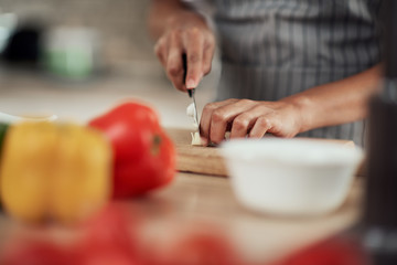 Wall Mural - Close up of mixed race woman in apron standing in domestic kitchen and cutting garlic.