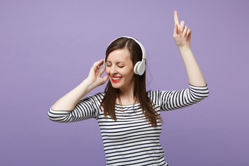 Young brunette woman girl in casual striped clothes posing isolated on violet purple background studio portrait. People sincere emotions lifestyle concept Mock up copy space Listen music in headphones