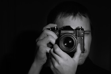 black and white portrait of a photographer with an old camera in his hands on a dark background.hori