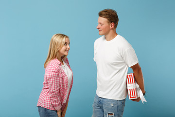 Wall Mural - Young pretty couple two friends guy girl in white pink t-shirts posing isolated on blue background. Valentine's Day, Women's Day, birthday concept. Hold red striped present box with gift ribbon bow.