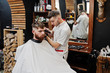 © AS Photo Family - Young bearded man getting haircut by hairdresser while sitting in chair at barbershop. Barber soul.