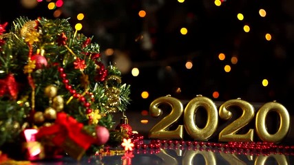 Wall Mural - Gold inscription 2020, decorated wreath, presents, decor are on table. Festive decorative garland with multicolored light bulbs, lanterns are blinking on background. New year, christmas mood.