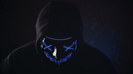 Man with lighting neon glow mask in hood on black background. Halloween and horror concept