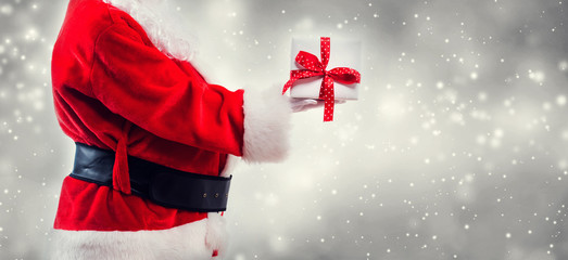 Wall Mural - santa holding a christmas gift on a shiny light background