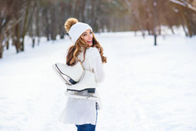 Beautiful Woman Weared In White Sweater And Hat With Ice Skates On The Back Walks In Winter Snowy Park.