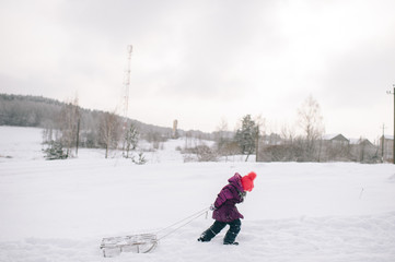 Wall Mural - Little child pulling sled up the snowy hill in cold winter day.