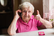 © De Visu - An elderly woman talks on a mobile phone sitting at his home.