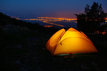 Wall Mural - orange lighted inside tent on mountain above city in night lights