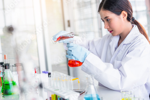Fotomural Attractive scientist woman looking chemical sample in flask at laboratory with lab glassware background