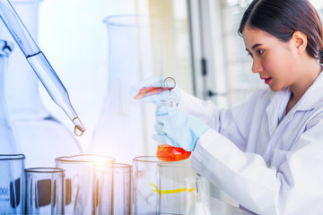 Canvas Print - Attractive scientist woman looking chemical sample in flask at laboratory with lab glassware background. Science or chemistry research and development concept.