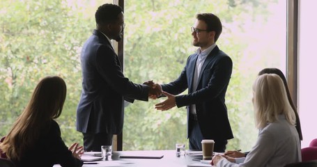 Wall Mural - Proud african manager promoting handshaking caucasian employee at team meeting