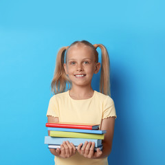 Wall Mural - Portrait of cute little girl with books on blue background. Reading concept