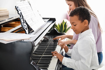 Wall Mural - Woman teaching little African-American boy to play piano at home