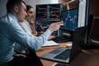 Man talks and shows on the numbers on monitor with hand. Team of stockbrokers are having a conversation in a office with multiple display screens