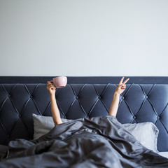 Wall Mural - good morning concept - female hands with coffee and victory sign sticking out from the blanket