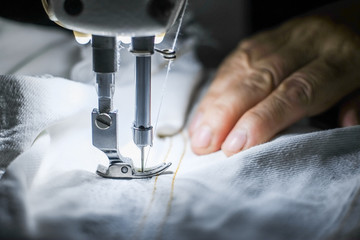 Hand of the seamstress is using a white industrial sewing machine to sew cloth.