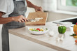 © nenadaksic - Close up of mixed race woman in apron putting chopped mushrooms in bowl with vegetables. Kitchen interior.