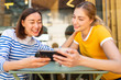 © mimagephotos - Happy mother and daughter sitting at cafe looking at cellphone together