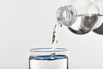 clear fresh water pouring into glass from bottle isolated on white