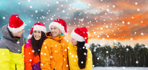 Poster - holidays, christmas, friendship and people concept - happy friends in santa hats and ski suits over winter forest background