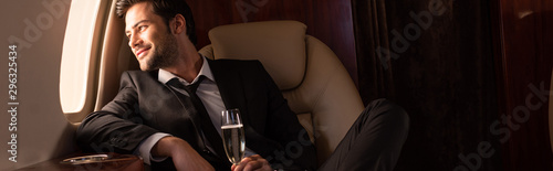 Fotomural handsome cheerful man holding glass of champagne in plane