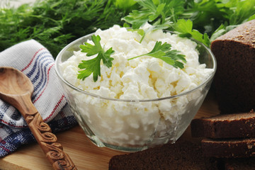 A bowl with cottage cheese, a bunch of green and rye bread	