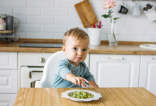 Charming Little Baby Boy Eating First Food Green Grape At Bright Kitchen At Home