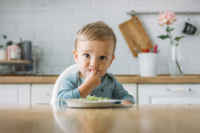 Charming Little Baby Boy Eating First Food Green Grape At The Bright Kitchen At Home