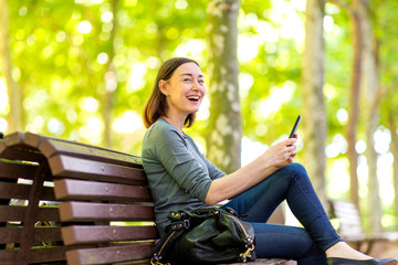 Wall Mural -  happy older woman sitting in park with mobile phone