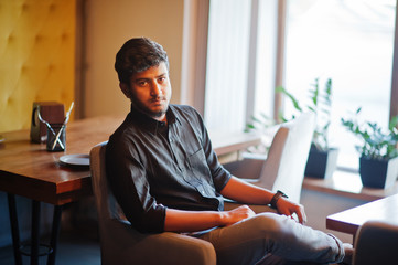 Wall Mural - Confident young indian man in black shirt sitting at cafe.