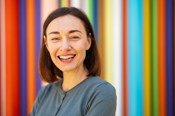 Close up beautiful middle aged woman smiling by colorful background