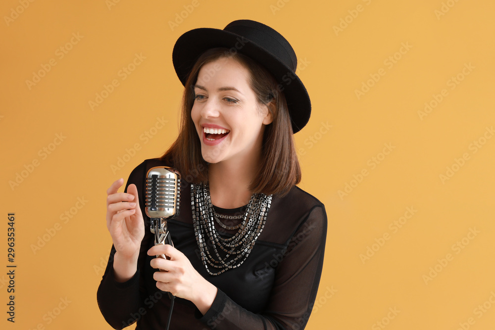 Beautiful young female singer with microphone on color background