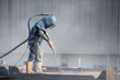 © sakarin14 - Sand blasting process, Industial worker using sand blasting process preparation cleaning surface on steel before painting in factory workshop.