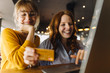 © Kniel Synnatzschke/Westend61 - Two happy female, friends with laptop and credit card in a cafe